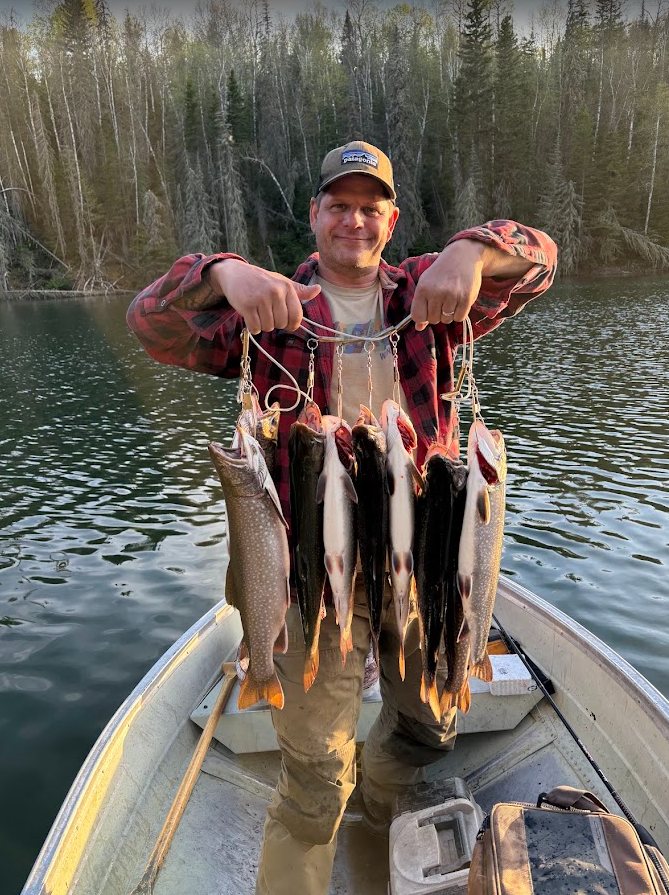 Dan Demers in a boat on a lake, holding up the day’s catch of fish